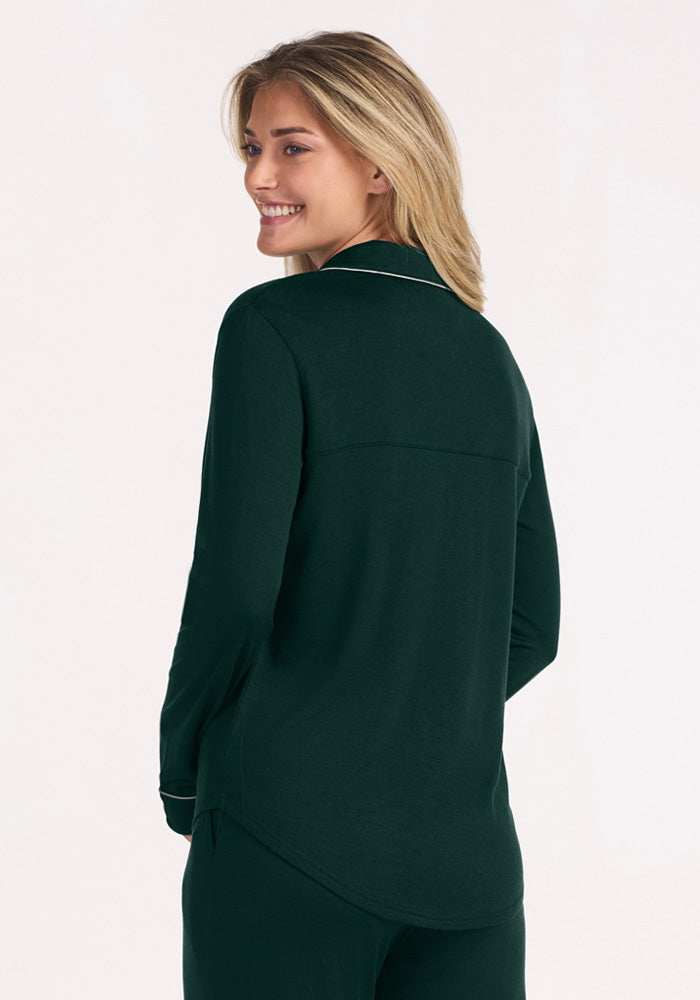 A smiling woman in a deep pine Woolx Harper FeatherTouch® Pajama Set, featuring a dark green long-sleeve top with piping.