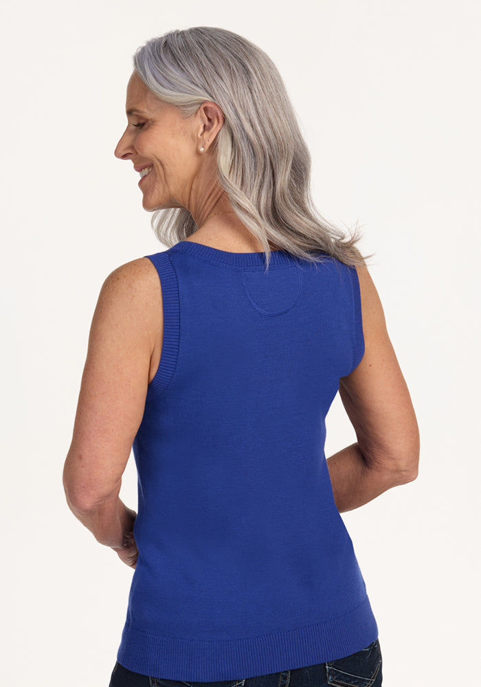 A smiling woman with long gray hair is seen from the back, wearing the Woolx Chessy Tank Top in royal blue and dark jeans, standing against a plain light background.