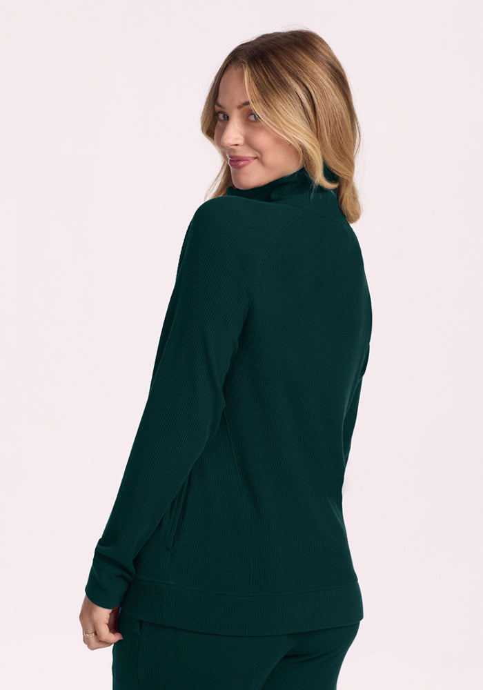 Woman in a Woolx Quinn Ribbed 1/4 Zip - Deep Pine smiles over her shoulder against a light background.