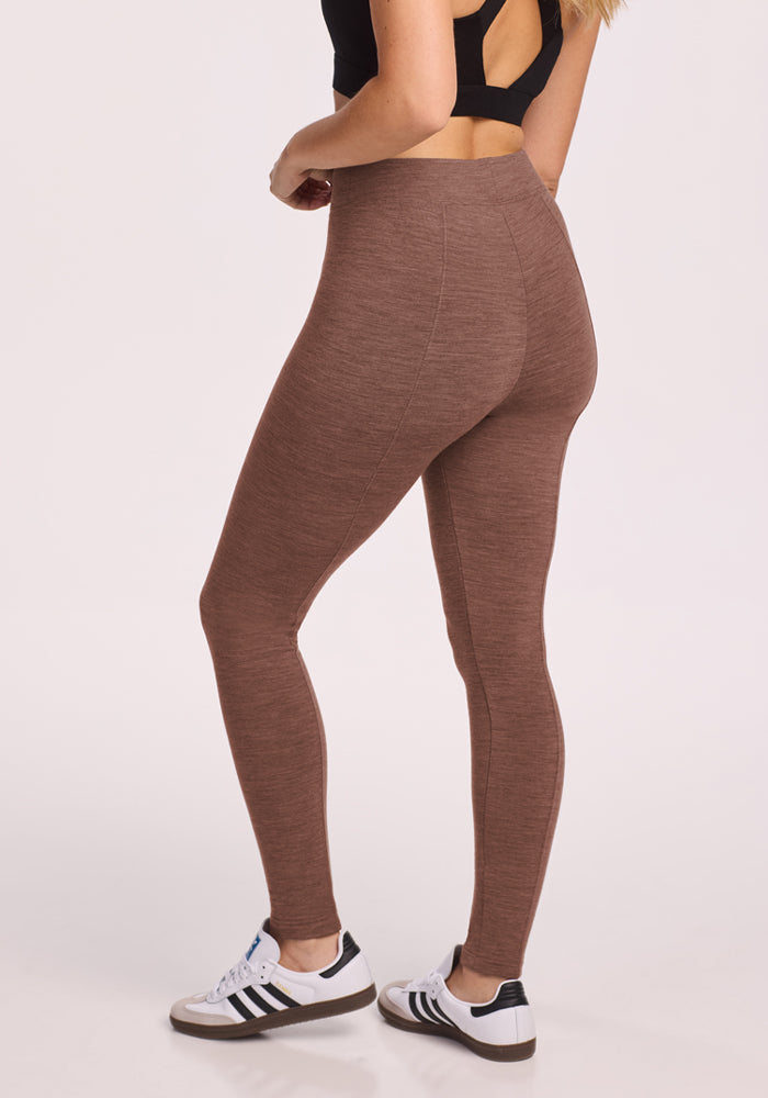 Woman in Woolx Stella Leggings - Sable Heather, black sports bra, and white sneakers stands against a light background.