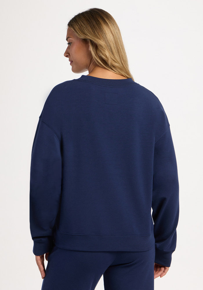 Back view of a person wearing a dark blue Woolx Molly Crewneck - Ocean Cavern merino wool sweater.