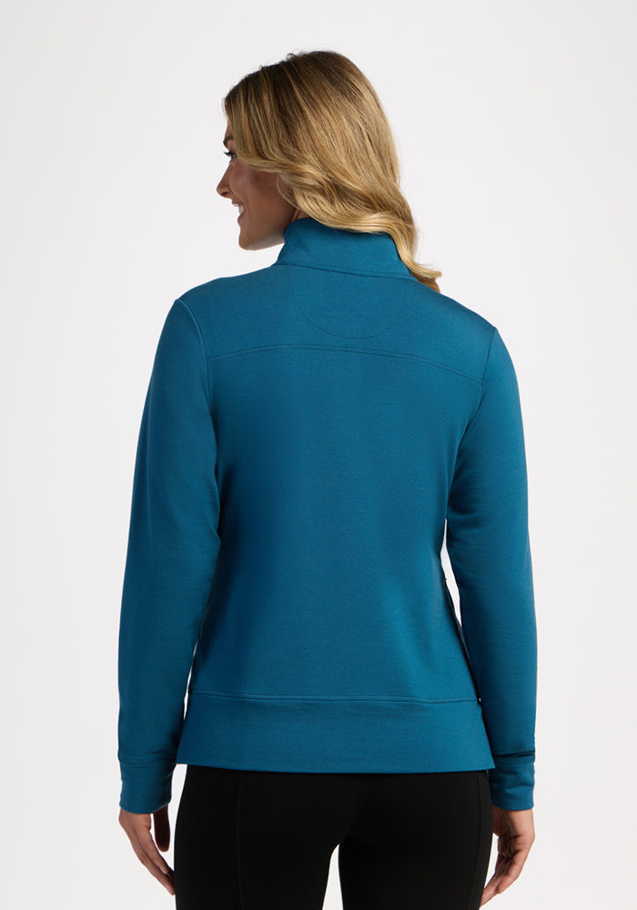 Woman with blonde hair in a Woolx Annie 3 Button Pullover - Blue Pine, black pants, seen from the back.