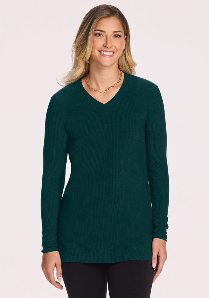 Woman in the Woolx Evie Ribbed Tunic in Deep Pine and black pants, standing and smiling against a light background. 