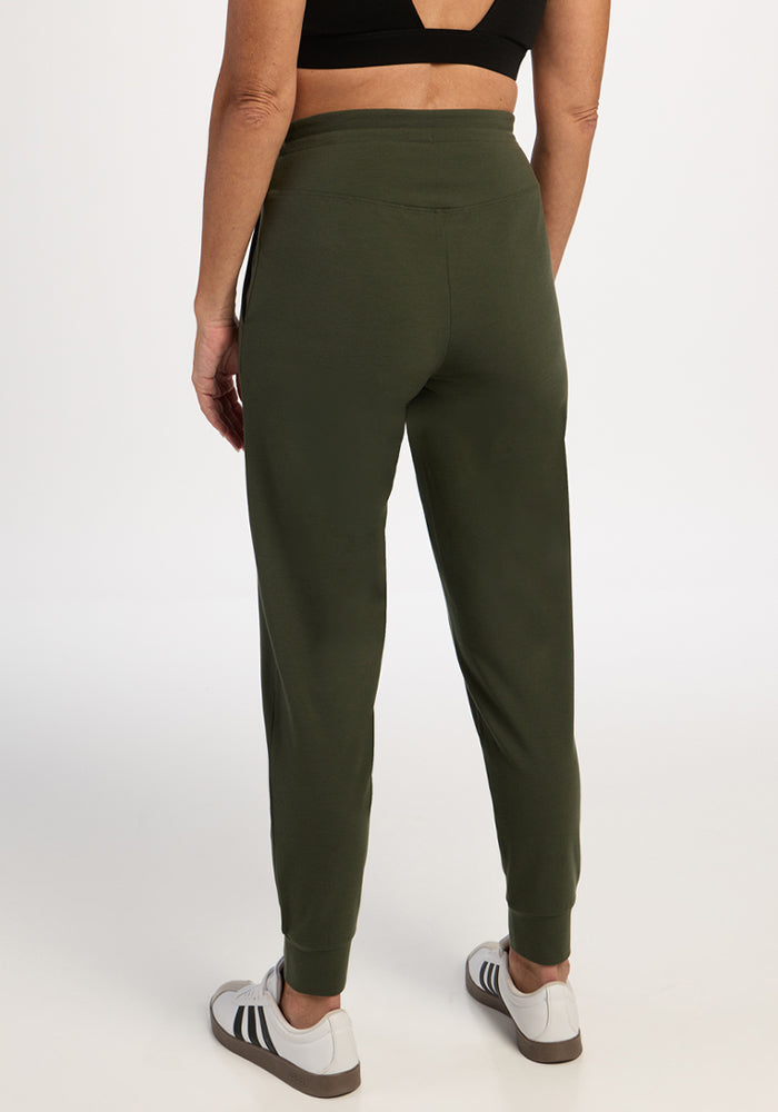 Person wearing Woolx Madden Petite Joggers in Everleaf, a black sports bra, and white sneakers, facing away.