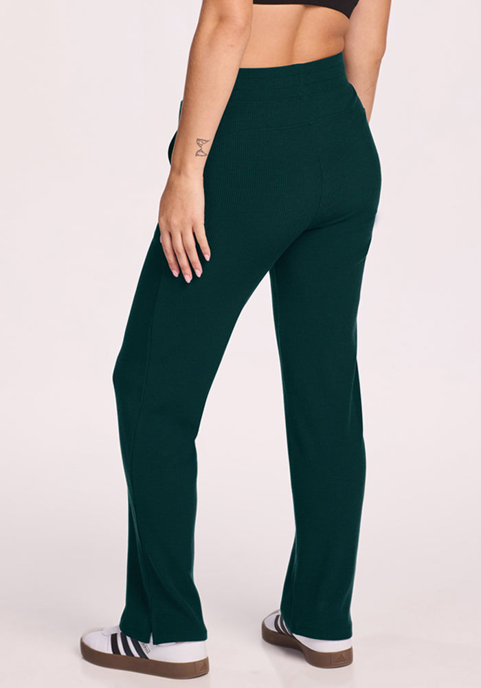 Person wears Woolx Luca Ribbed Pants - Deep Pine, black sports bra, and white sneakers with black stripes.