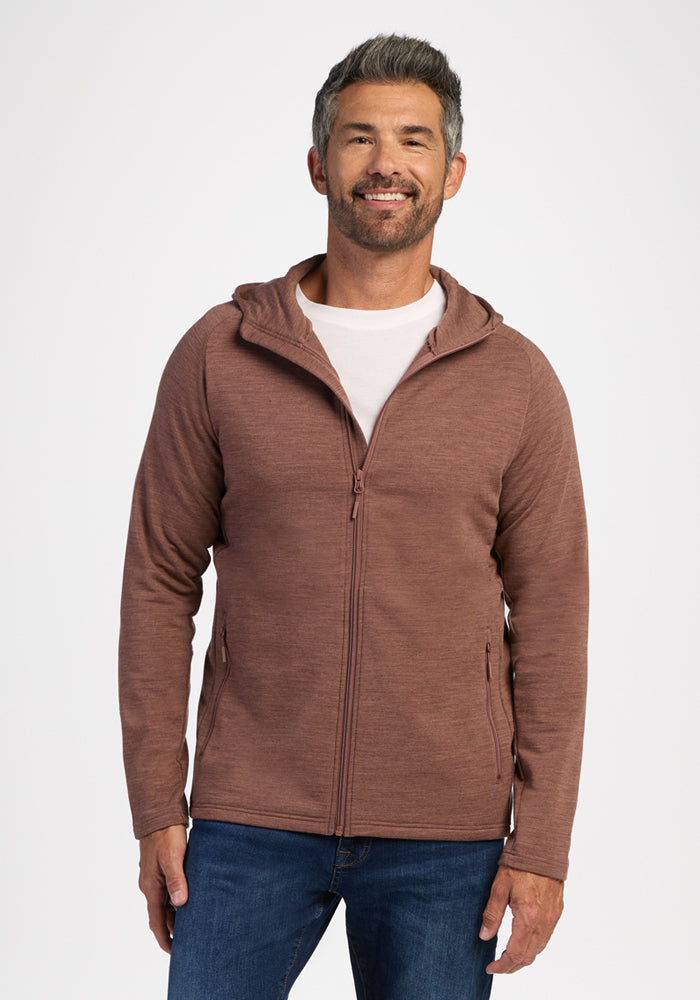 Man in a Woolx Boulder Hoodie - Sable Heather and jeans stands smiling against a plain white background. 