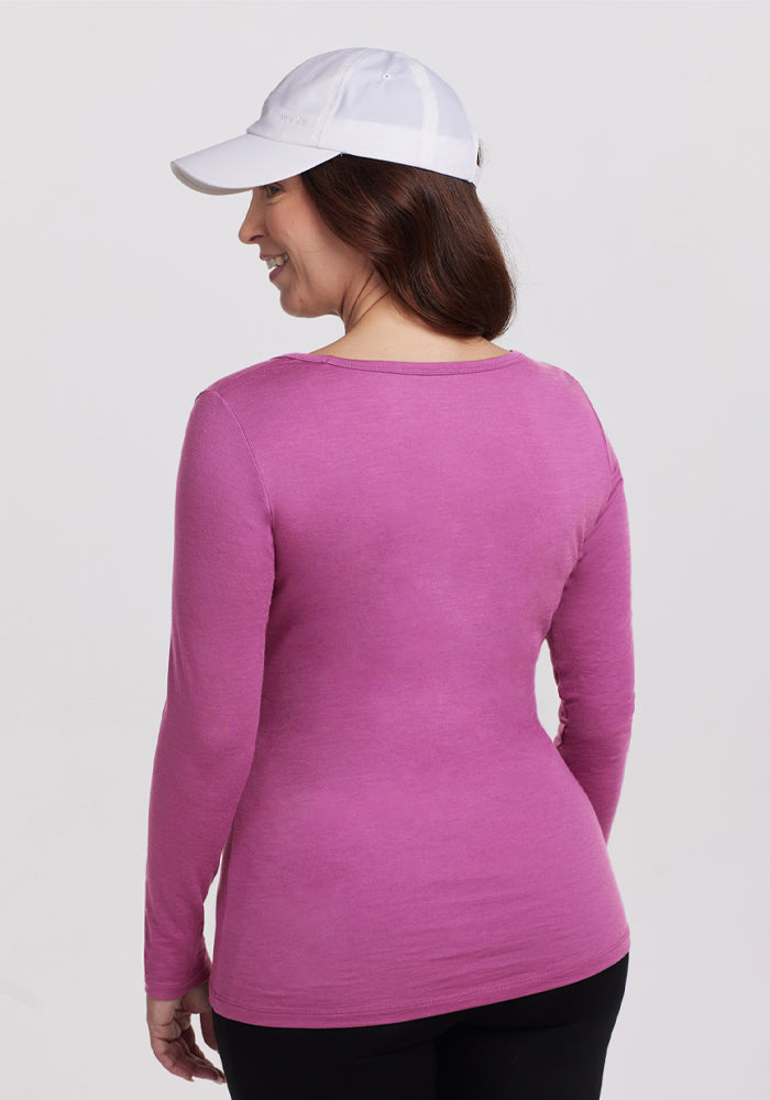 A woman is shown from the back, wearing a white baseball cap and the Woolx Layla V Neck Top in Purple Wine, standing against a plain light background.