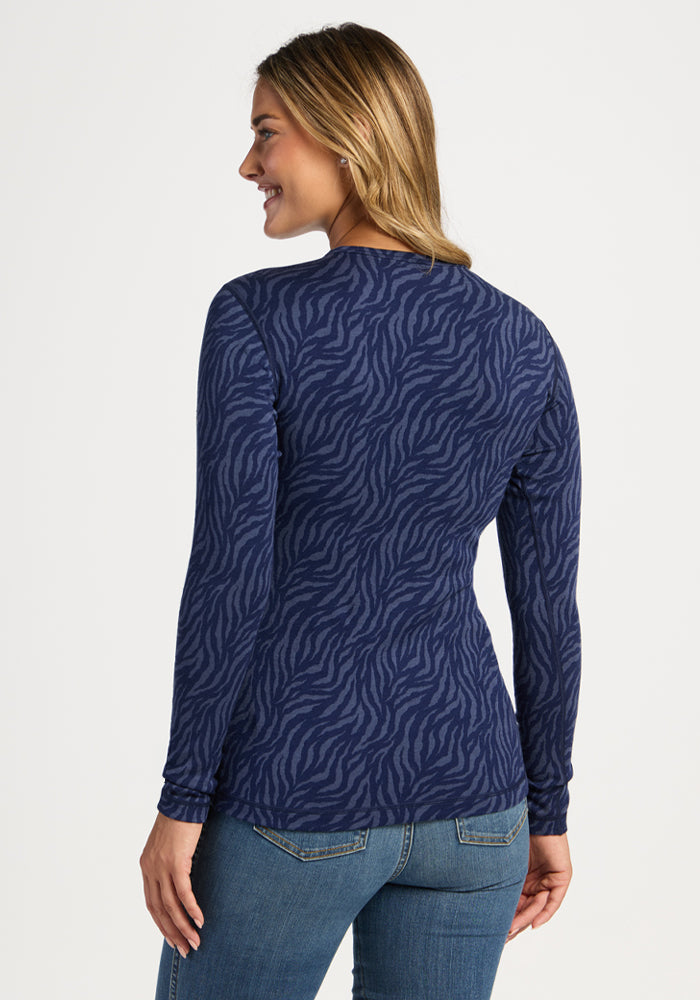 Woman in Woolx Maddie Baselayer Top - Midnight Safari, smiling in jeans, looking over her shoulder against white backdrop.