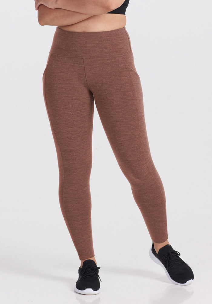 Model wears Woolx Piper Pocket Leggings in Sable Heather with a black top and sneakers, arms crossed, on white background.
