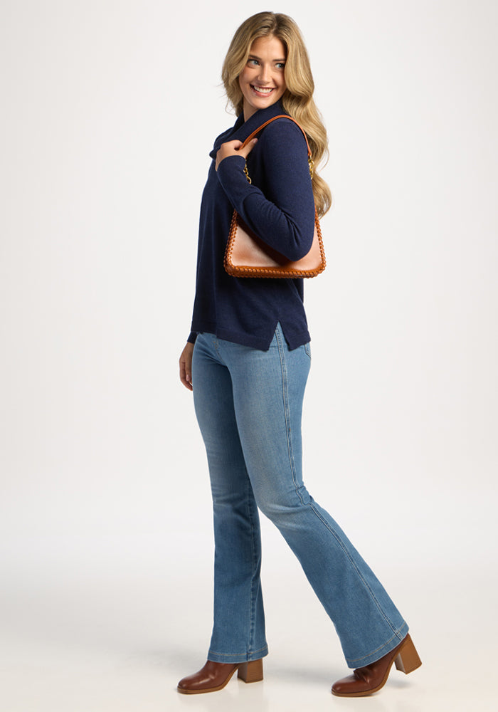 Woman smiling in Woolx Josie Cowl Neck Sweater - Ocean Cavern, blue jeans, brown boots, and a brown handbag.