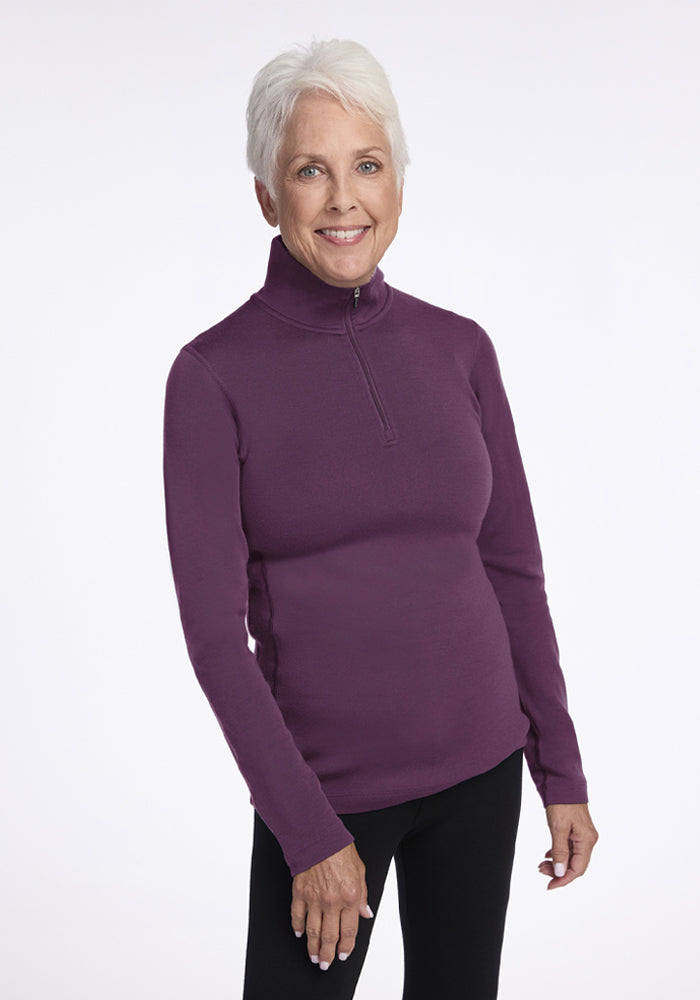 Older woman with short white hair smiles, wearing a Woolx Brooke 1/4 Zip in Purple Iris and black pants. 