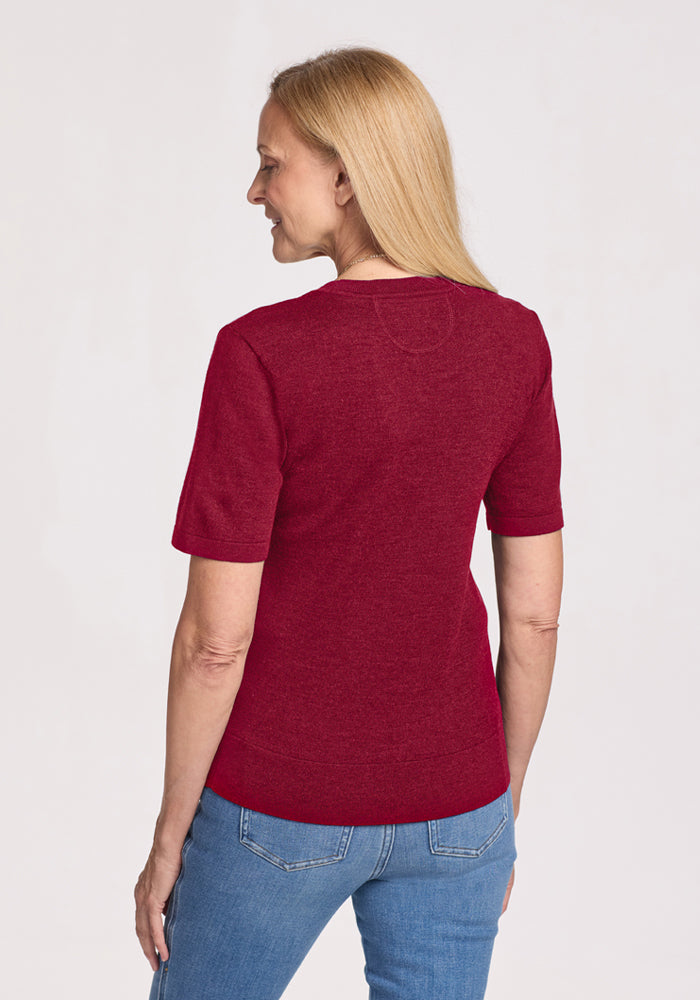 Woman with long blonde hair wears the Woolx Anna Crew Sweater - Beet Red and blue jeans, facing away and smiling.