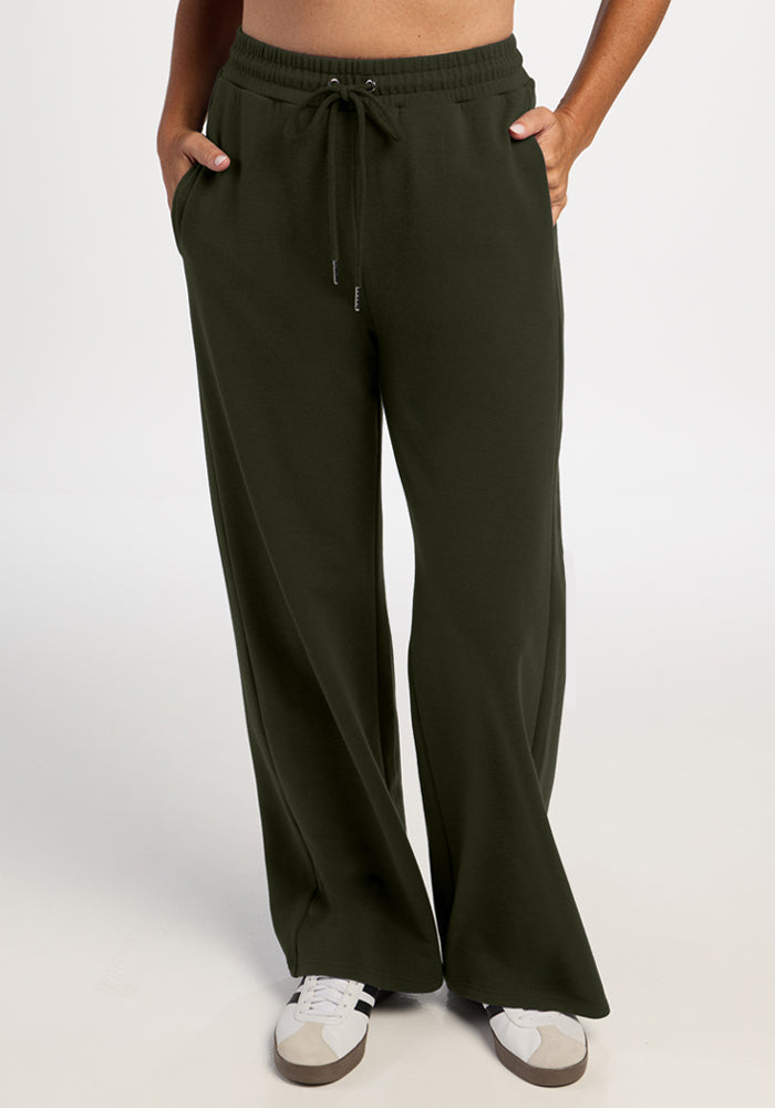 Someone in Woolx Eloise Wide Leg Pants - Duffel Bag and white sneakers stands hands-in-pockets, exuding relaxed style. 
