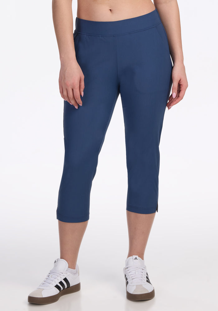 A person models the Woolx Nicole Crop Pants in Vintage Indigo, paired with white sneakers with black stripes, standing against a plain white background. Only the lower torso and legs are shown. 