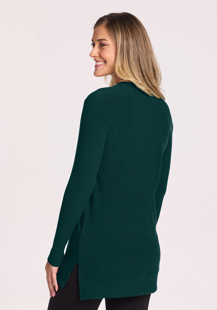 Woman in Woolx Evie Ribbed Tunic - Deep Pine, smiling, standing with her back slightly to the camera.