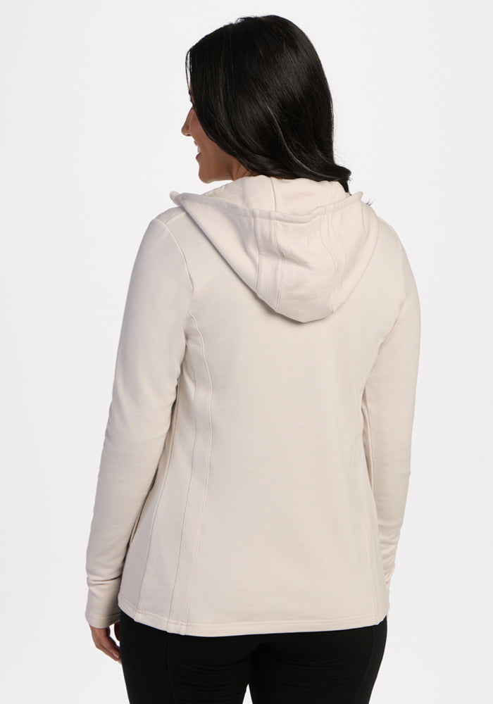 Woman facing away, wearing Woolx Zoey Zip Up Hoodie in Ecru and black pants against a plain white background.
