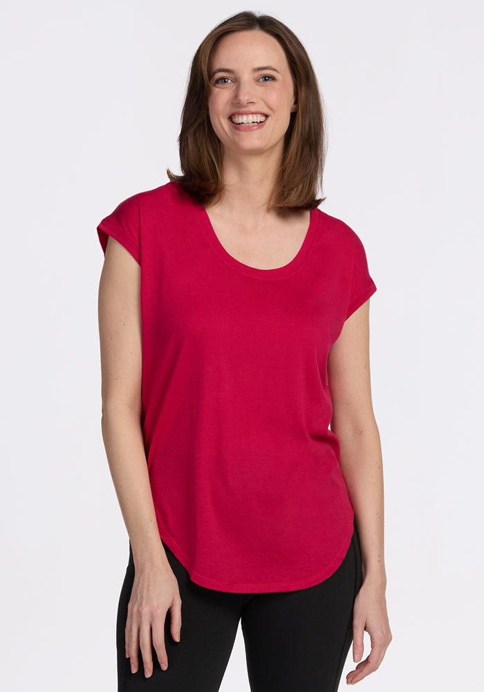 A woman with shoulder-length brown hair, wearing the Woolx Gabi Tunic Top in Poppy Spark and black pants, smiles against a plain white background. 