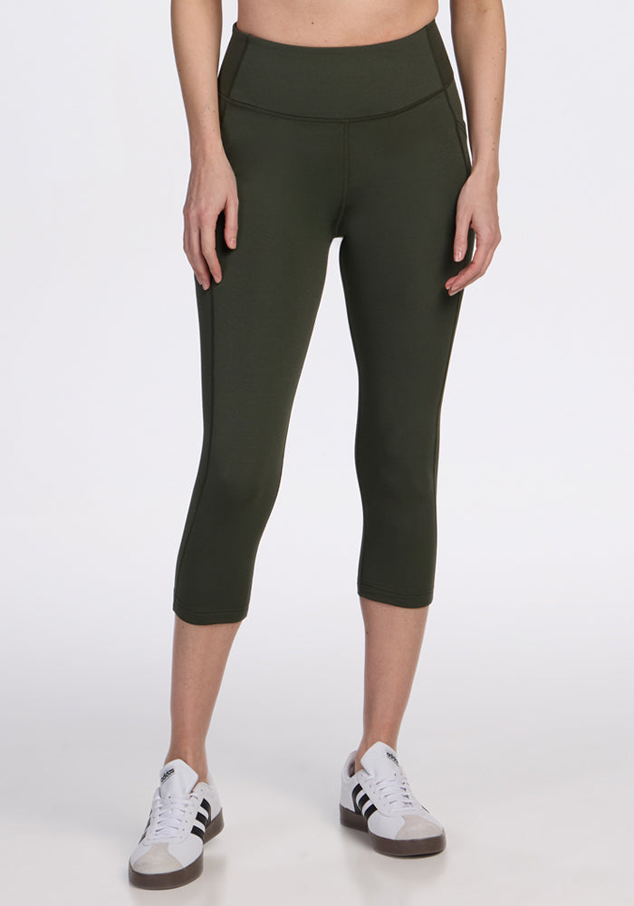 A person wears Woolx Merino Flex® McKenna Capris in Everleaf, featuring a high-waisted, comfortable, moisture-wicking merino wool blend—ideal for all-day wear—paired with white sneakers with black stripes against a white background. 