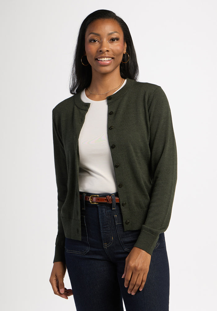 Smiling woman in the Woolx Caitlin Sweater - Duffel Bag, layered over a white shirt and jeans, on plain backdrop. | Jade is 5’10”, wearing a size S