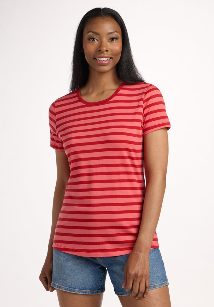 A woman with long dark hair smiles while wearing the Woolx Liza Crew Neck Tee in Wildberry Stripe and denim shorts, standing against a plain white background. 