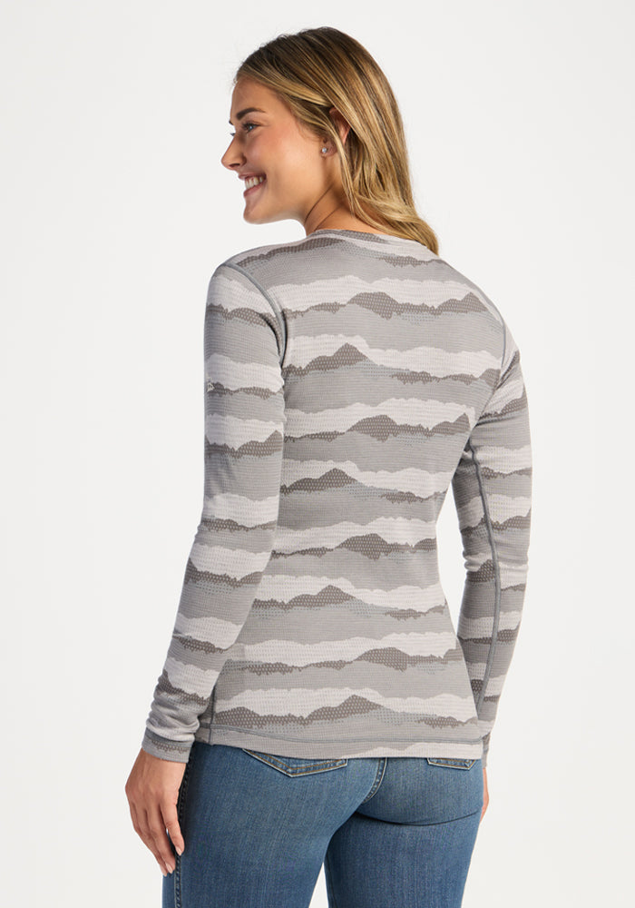 Smiling woman in Woolx Maddie Baselayer Top - High Peaks and blue jeans, looking over her shoulder.