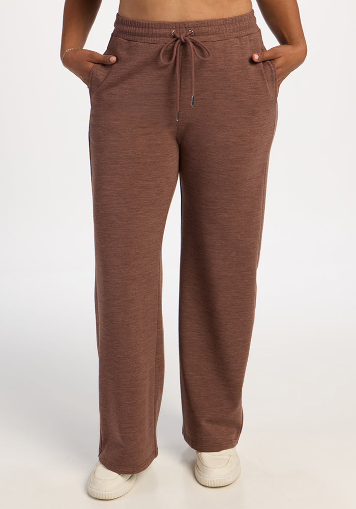 Model wears Woolx Eloise Wide Leg Pants in Sable Heather with white sneakers, hands in pockets, plain background. 