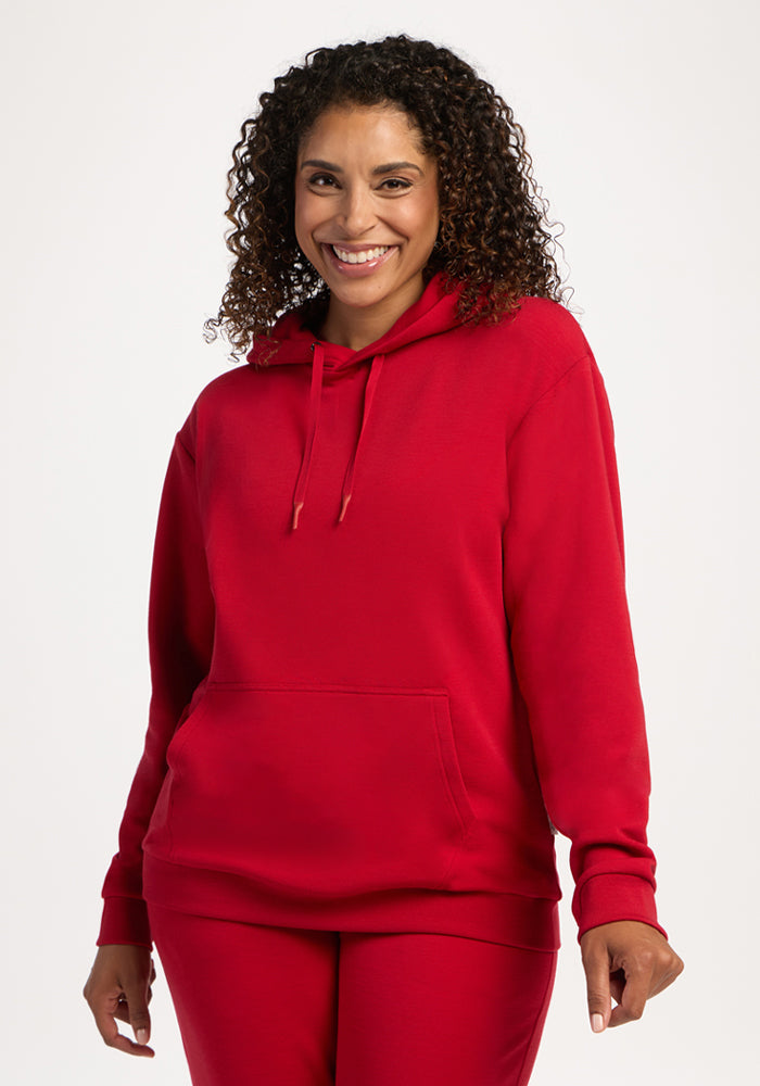 Smiling woman with curly hair wears the cozy Woolx Avery Hoodie - Maraschino Cherry and matching pants. 