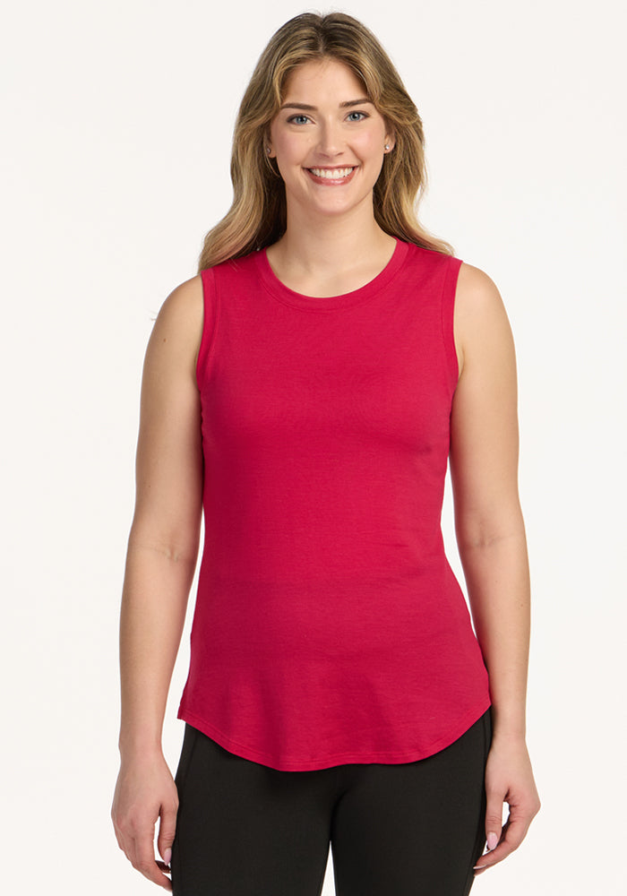 A woman with long, wavy blonde hair smiles while wearing the Woolx Bella Tunic Top in Poppy Spark and black pants, standing against a plain white background. 