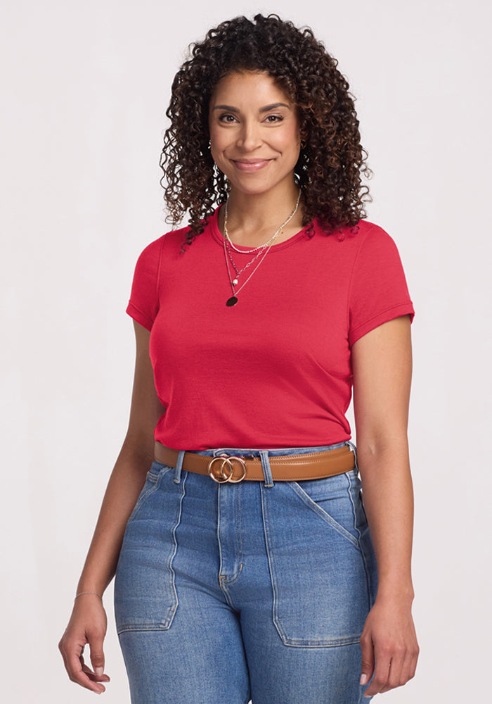 Smiling woman with curly hair wears Woolx Addie Crew Neck - Berry Ice Pop and blue jeans against a light background. 