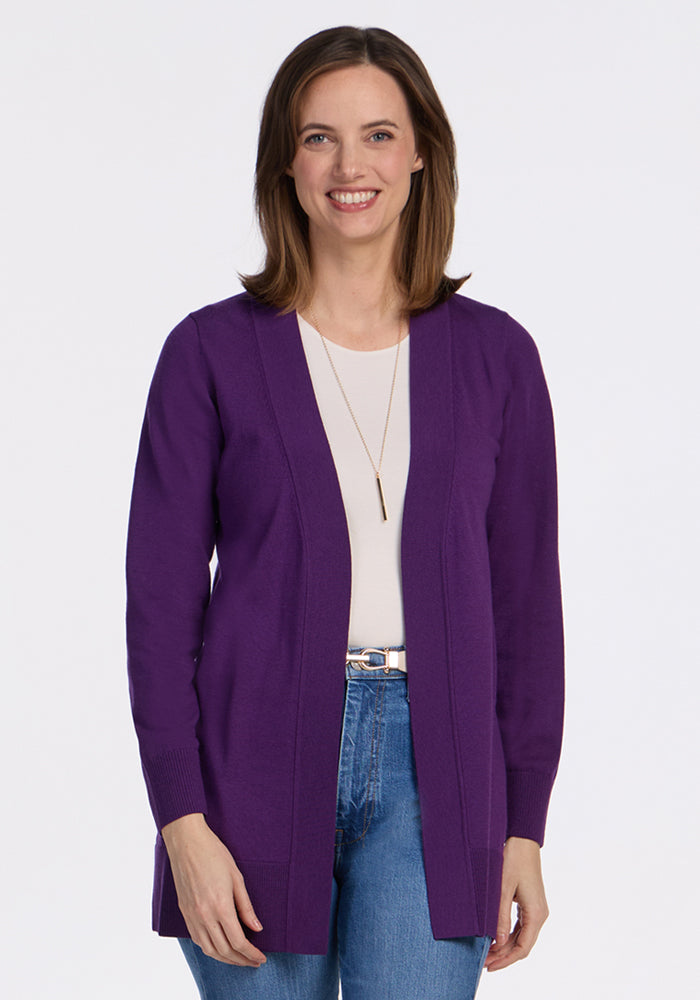 A woman with shoulder-length brown hair, wearing the Woolx Macie Sweater in Plum Crush over a white top and blue jeans, smiles against a plain white background. | Jessica is 5'10", wearing a size S