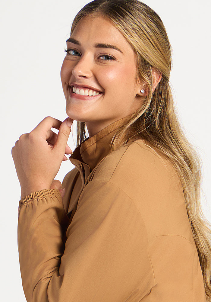 A smiling woman wearing a tan Cooper Windbreaker - Saddleback with a high collar.