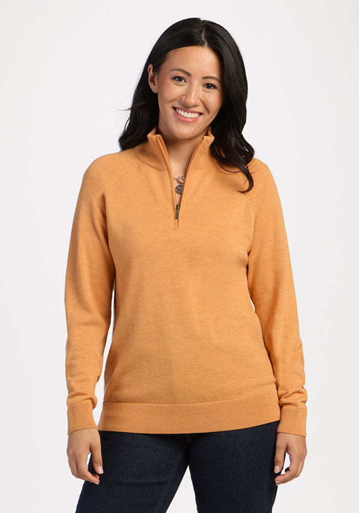 Woman in Woolx Collins Half Zip Sweater in Butterscotch and dark jeans, smiling against a white background. 