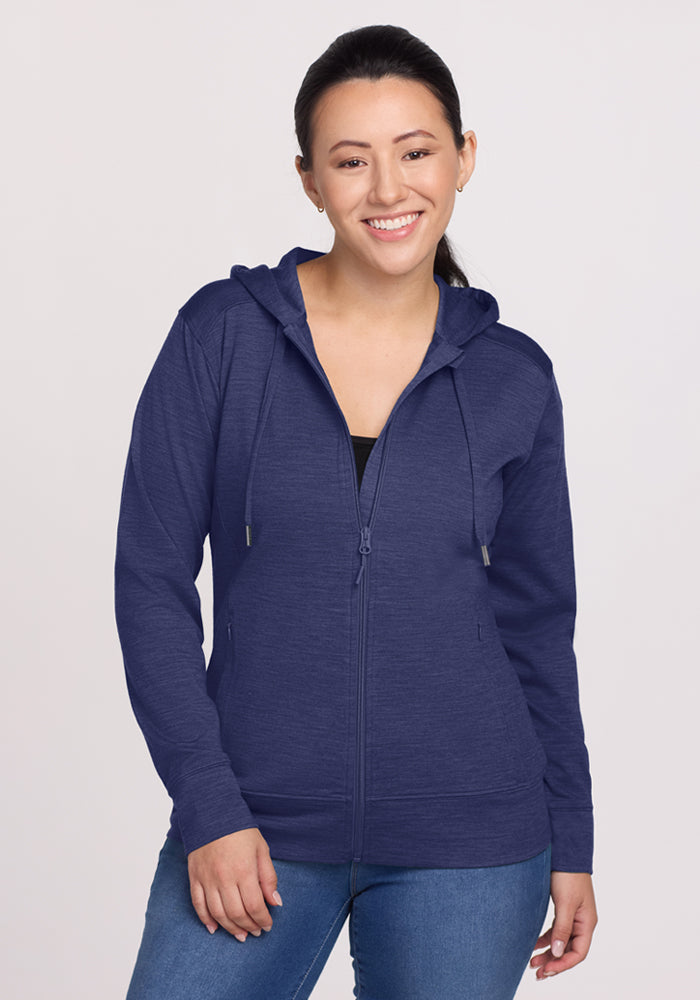 Woman models Woolx Ryann Hoodie in Twilight Storm with jeans, smiling—perfect travel essential against a light backdrop. | Sarah is 5'8", wearing a size S