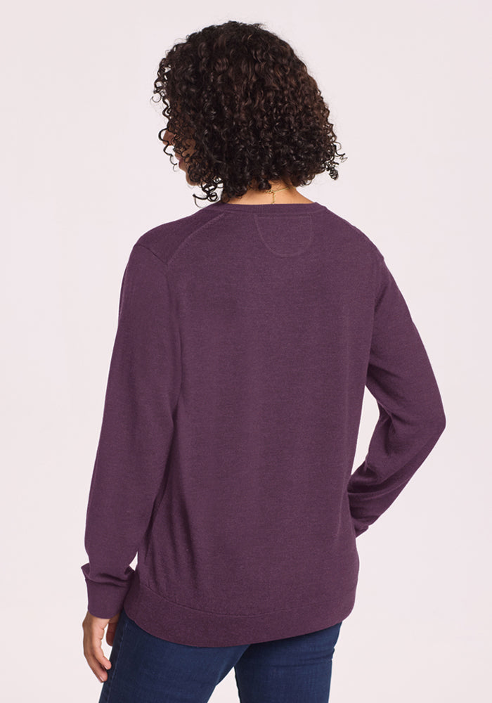 A person with curly hair wears the Woolx Francesca Sweater in Purple Iris and jeans, seen from the back.