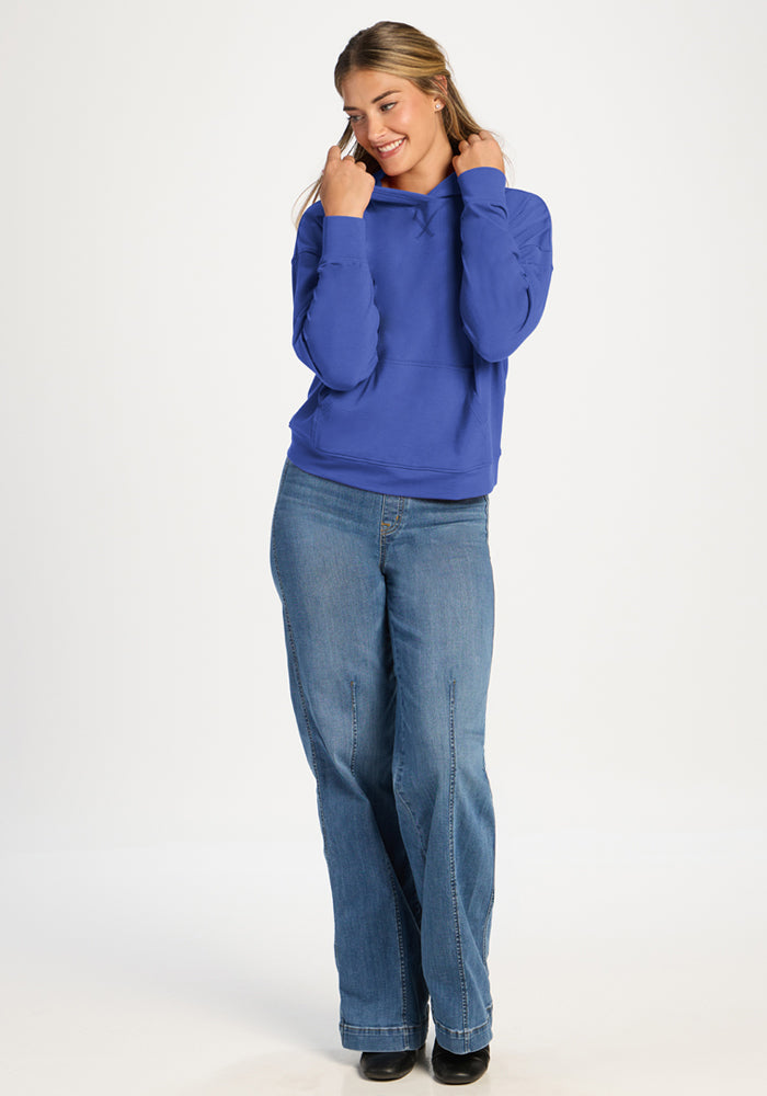 Woman in a Woolx Lizzy Hoodie - Royal Blue and jeans smiles with hands near her face, against a white background.
