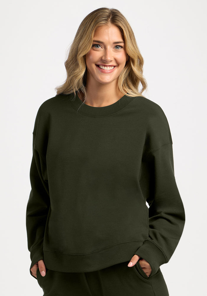 A woman smiles while wearing a dark green, moisture-wicking Molly Crewneck - Duffel Bag merino wool sweatshirt.
