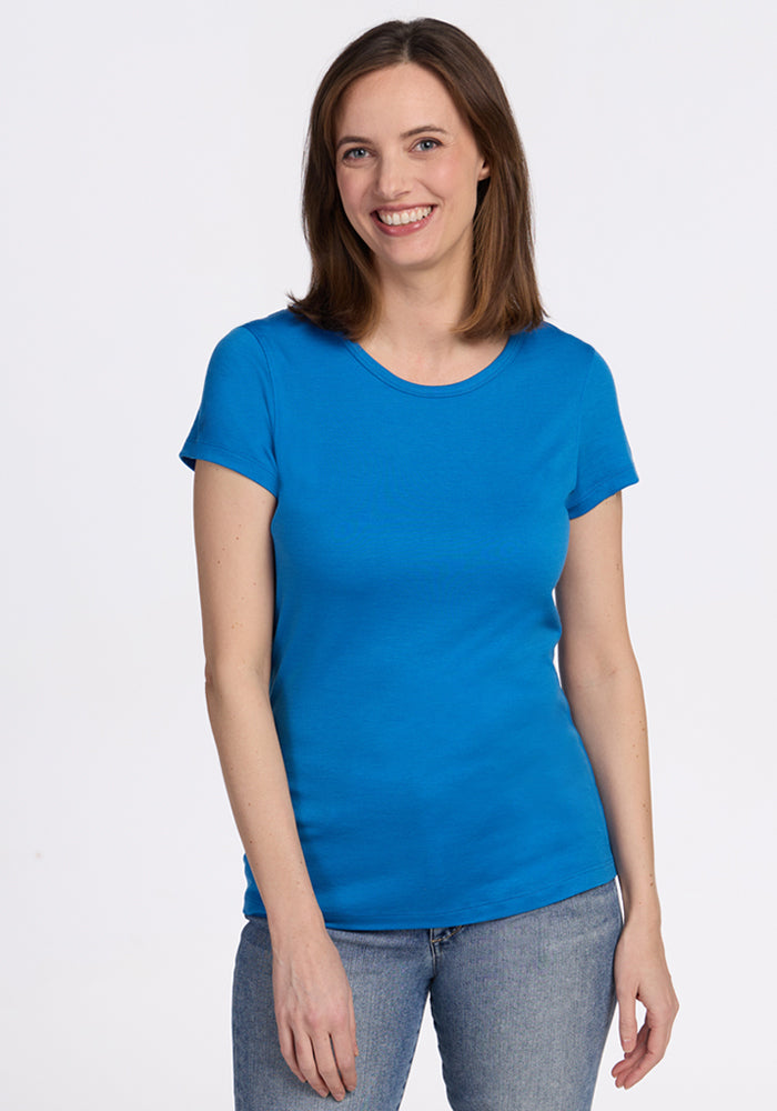 A woman with straight brown hair smiles against a plain white background, wearing the Woolx Addie Crew Neck - Wave Rider and light blue jeans. 