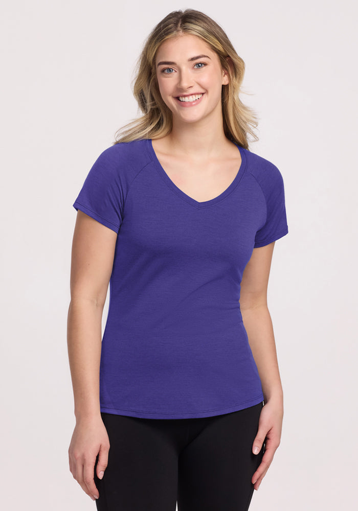 Smiling woman with long blonde hair wears the Woolx Mia V Neck - Berry Indigo tee and black pants against a light background. 