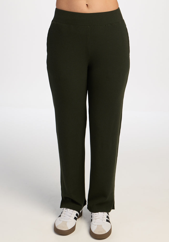 Person wearing Woolx Luca Ribbed Pants in Duffel Bag green with white sneakers, standing on a plain white background. 