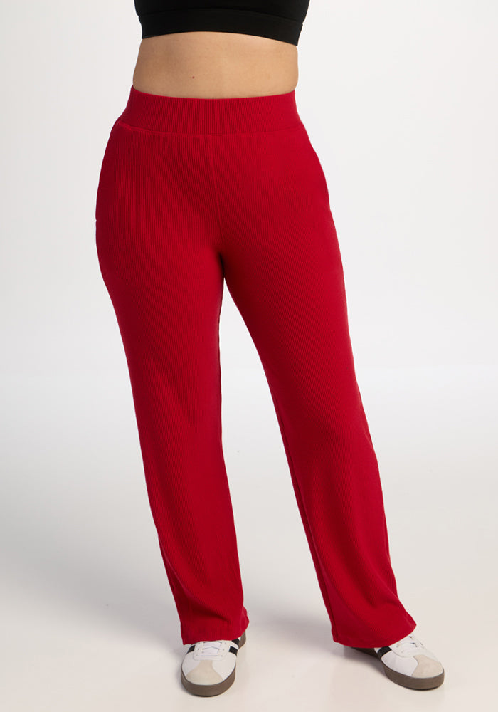 Model wears Woolx Luca Ribbed Pants in Maraschino Cherry with white sneakers and a black crop top against a white backdrop. 