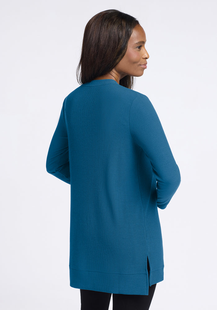 Woman facing away in Woolx Evie Ribbed Tunic - Blue Pine and black pants, on a plain white background.