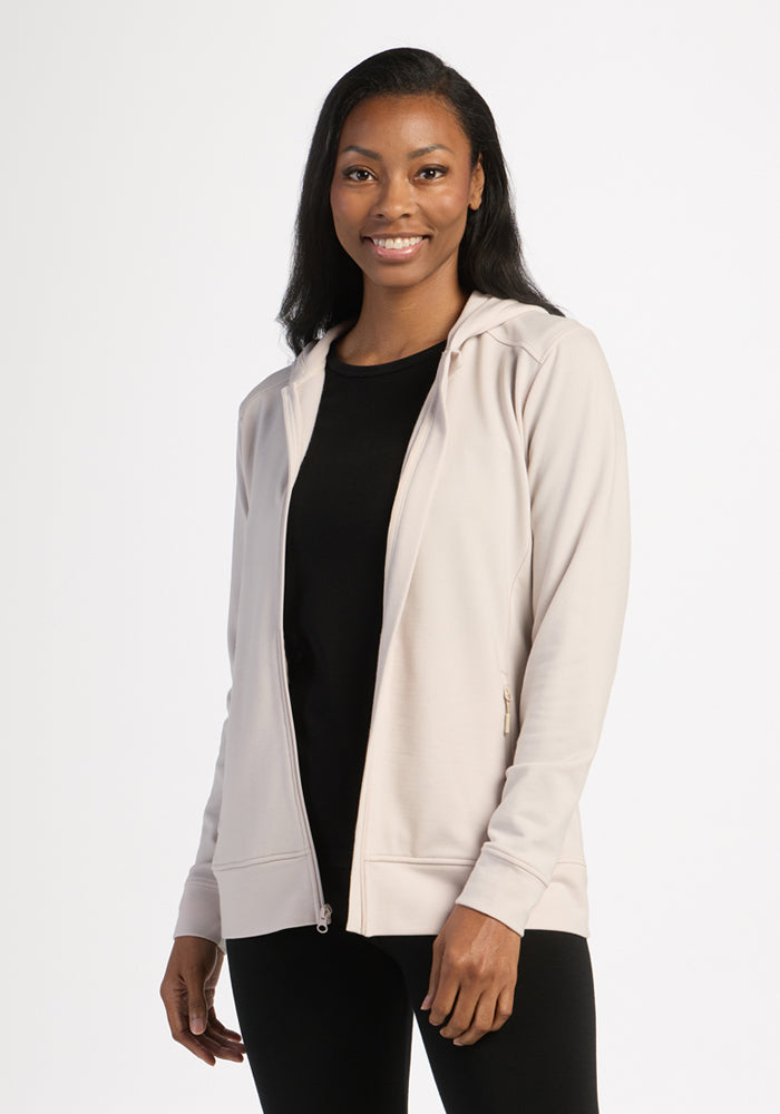 Woman smiling in a black shirt and Woolx Darby Zip Up Hoodie in Ecru, standing against a plain white background. 