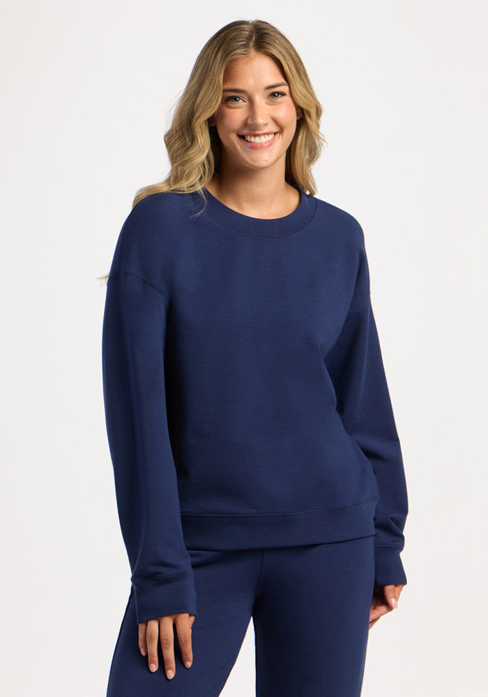 A woman smiles while wearing a dark blue Molly Crewneck - Ocean Cavern merino wool sweatshirt. 