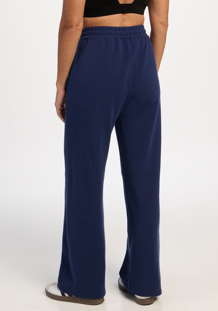 Person in Woolx Eloise Wide Leg Pants - Ocean Cavern, black crop top & slippers, seen from behind on white background.