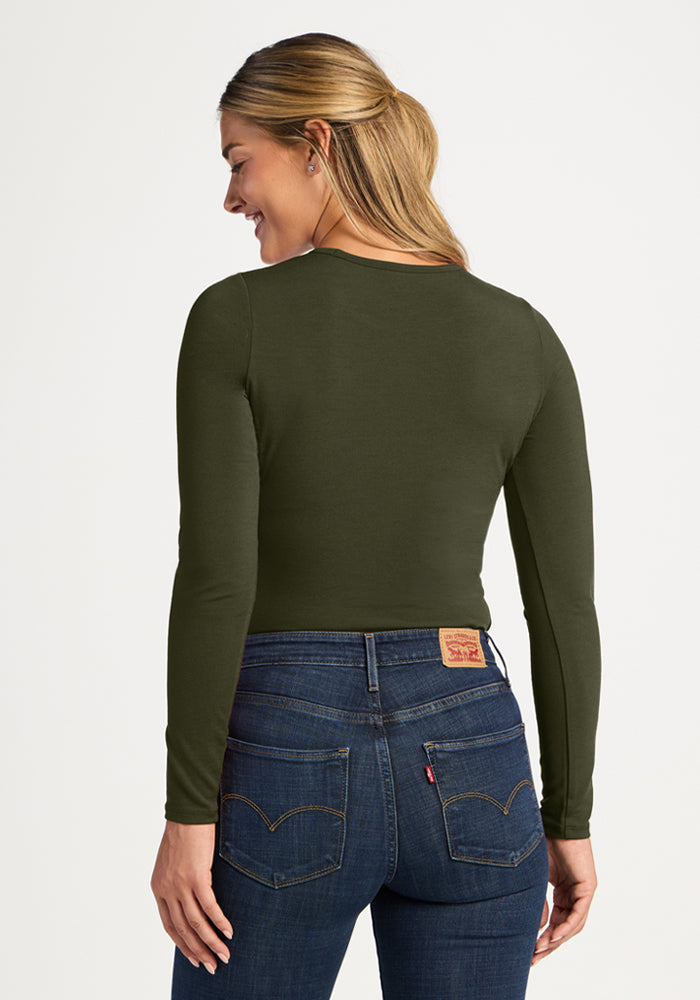 Woman in Woolx Margot Bodysuit - Everleaf and dark jeans, smiling over her shoulder.