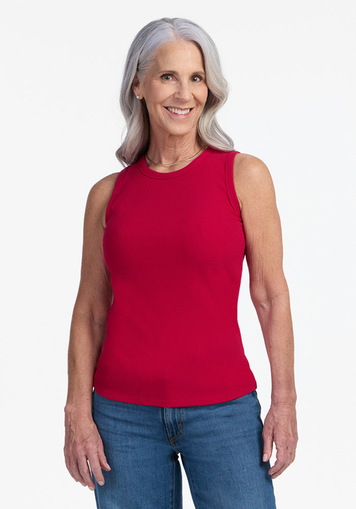 A smiling older woman with long gray hair wears the Woolx Raegan Ribbed Tank Top in Poppy Spark and blue jeans, standing against a plain white background facing the camera. 