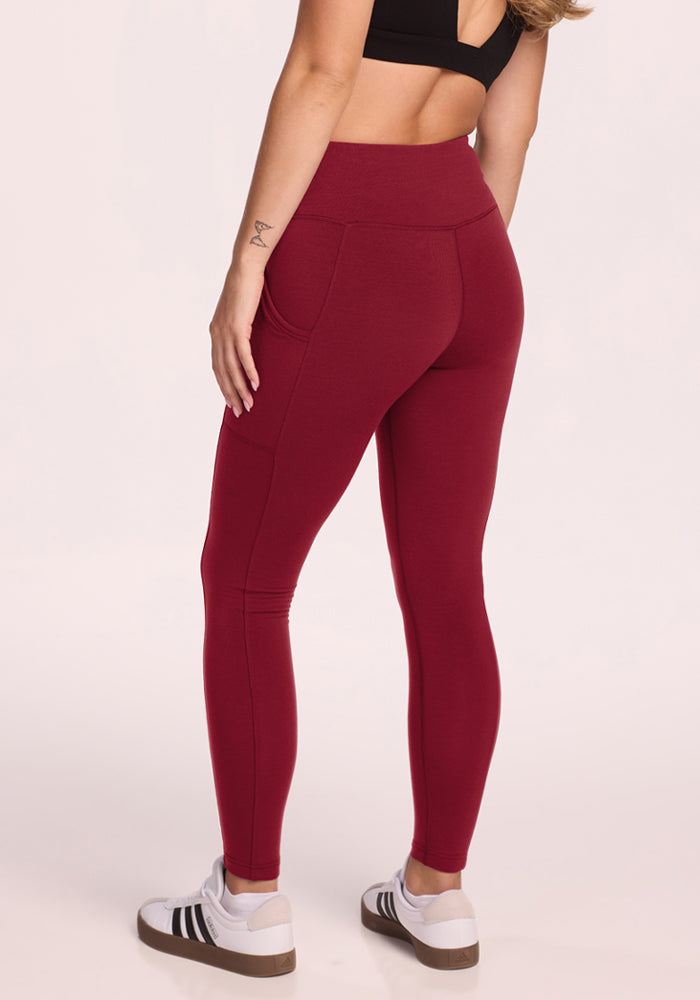 Woman wears Woolx Piper Pocket Leggings in Pinot Noir, a black sports bra, and white sneakers, back to the camera.