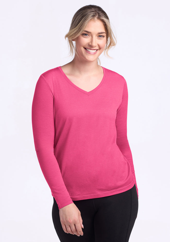 A blonde woman with her hair tied back is smiling, wearing the Woolx Millie Long Sleeve in Raspberry Fizz and black pants, standing against a plain light background. | Ariana is 5'11", wearing a size S