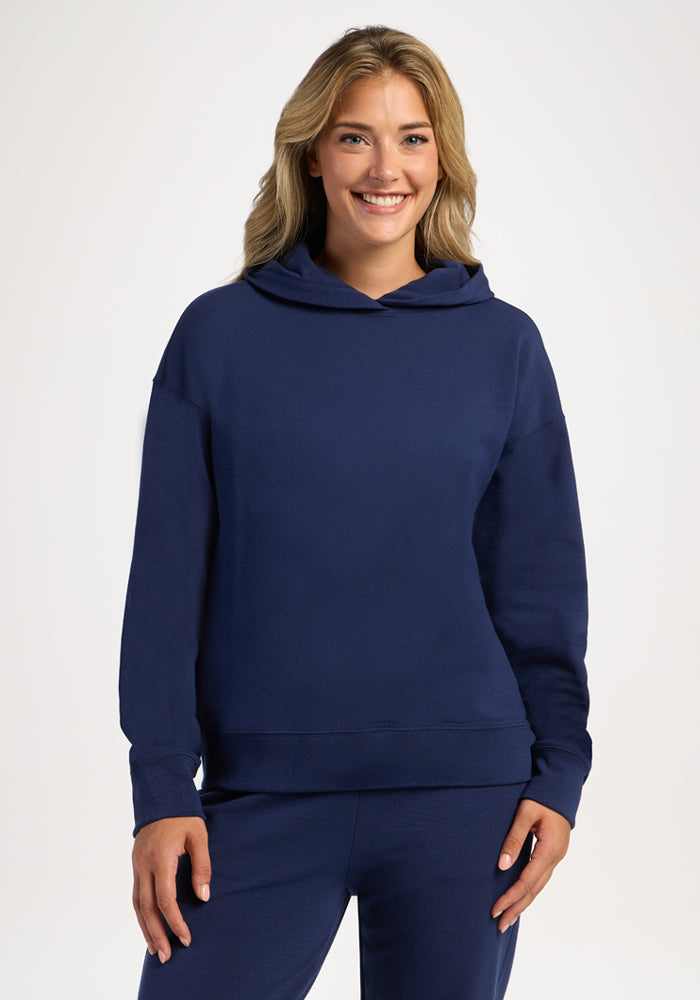 A smiling woman wearing a deep blue Genevieve Hoodie - Ocean Cavern in moisture-wicking merino wool. 