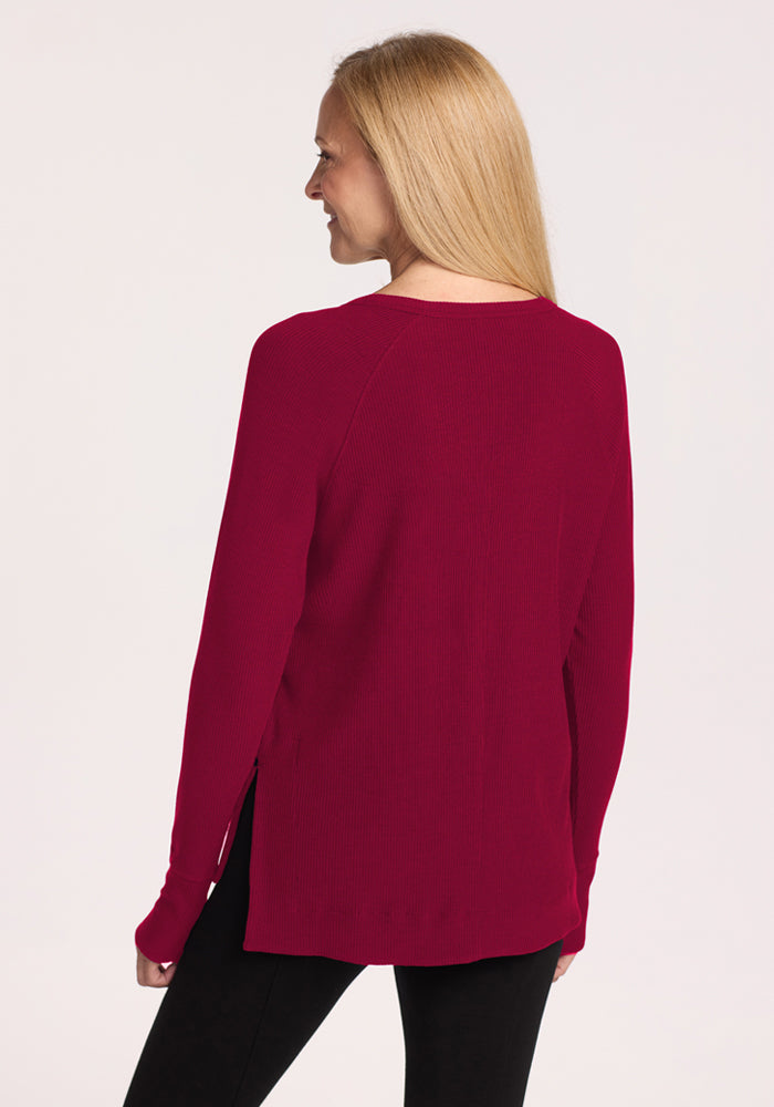 Woman in the Woolx Ainsley Sweater in Beet Red and black pants, smiling with her back to the camera.